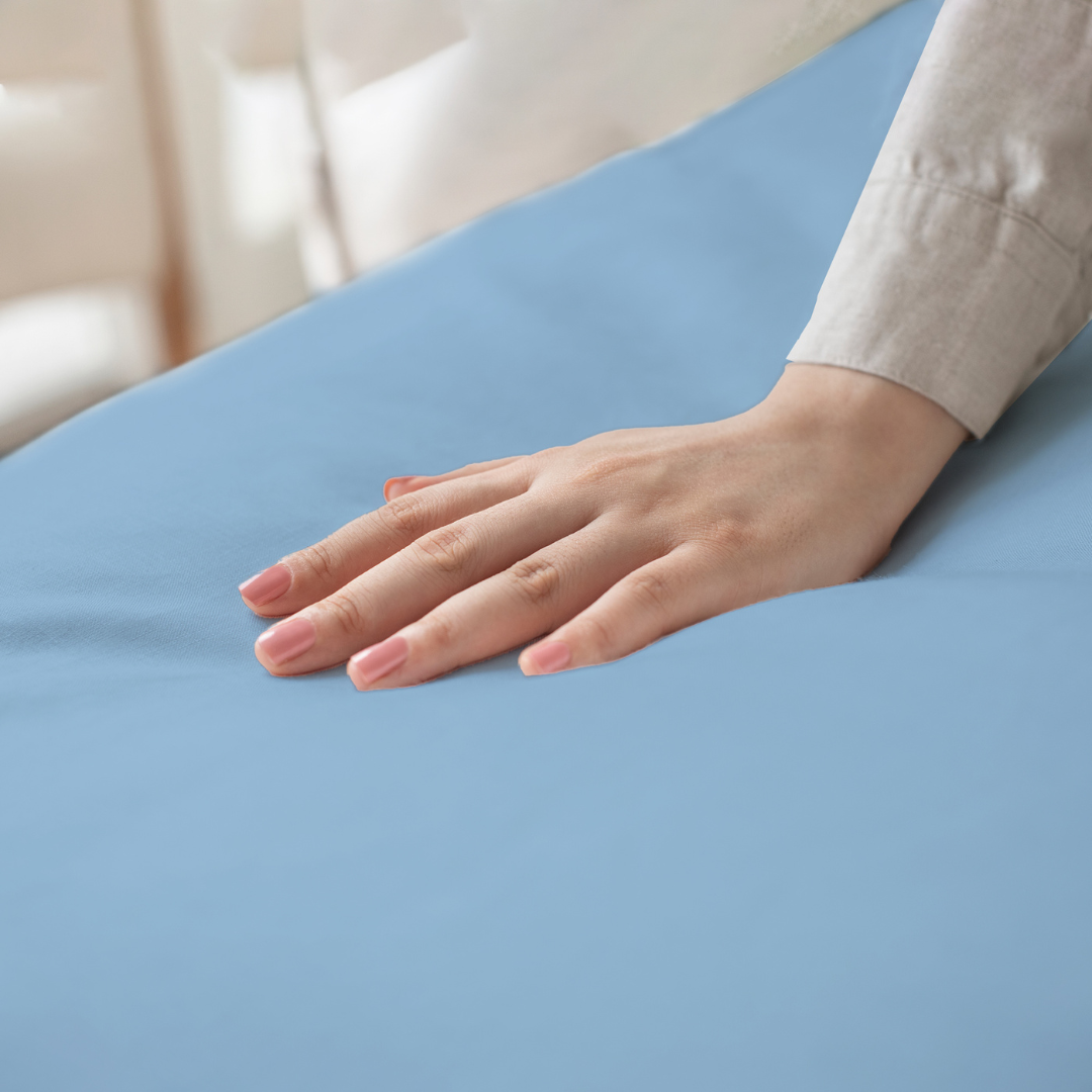 Hand feeling a soft, blue, 300 thread count Egyptian cotton king size bed sheet. This sheet set includes two pillowcases.