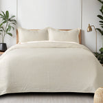 Milky white waffle-weave cotton bedspread with subtle texture on a made bed with two matching pillow shams.