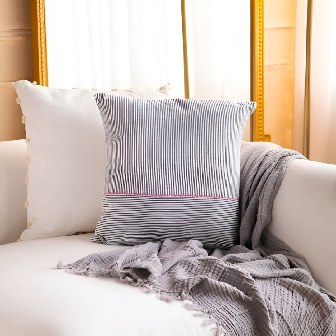 Black and white striped cushion cover with pink stitching, styled on a white sofa with a grey throw blanket.