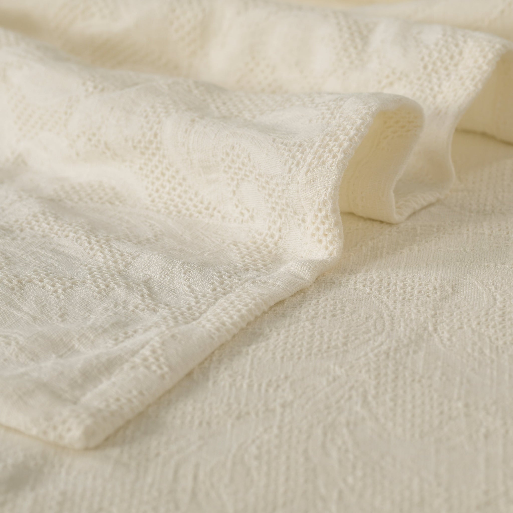 Milky white waffle-weave cotton bedspread with subtle woven pattern, shown draped for texture. Includes two matching sham covers.