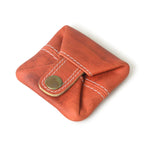 Stylish, orange leather mini wallet with white stitching and antique brass button closure, laying on a white background.