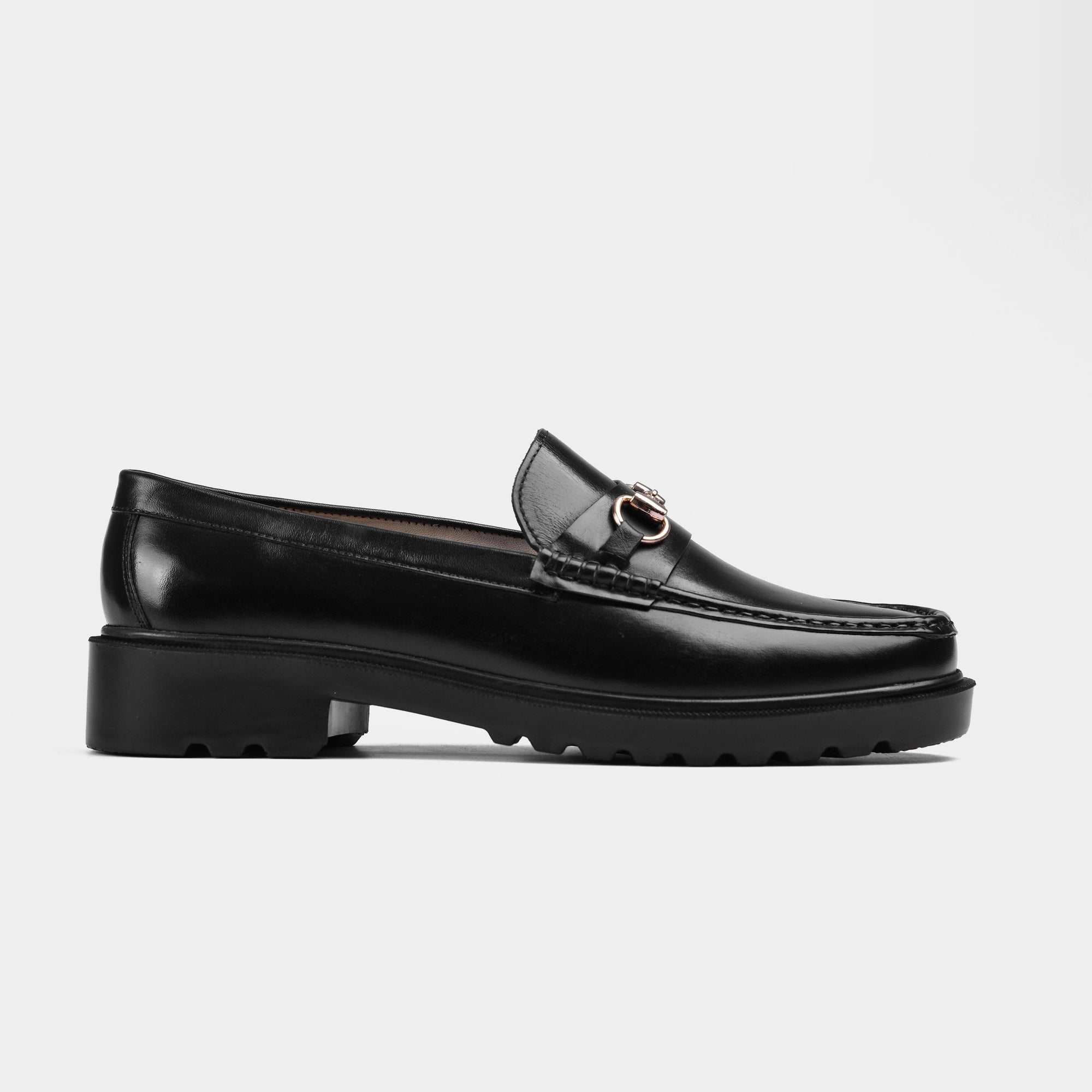 A pair of black leather loafers with a chunky sole and gold buckle detailing. Solesculpt Lite technology.