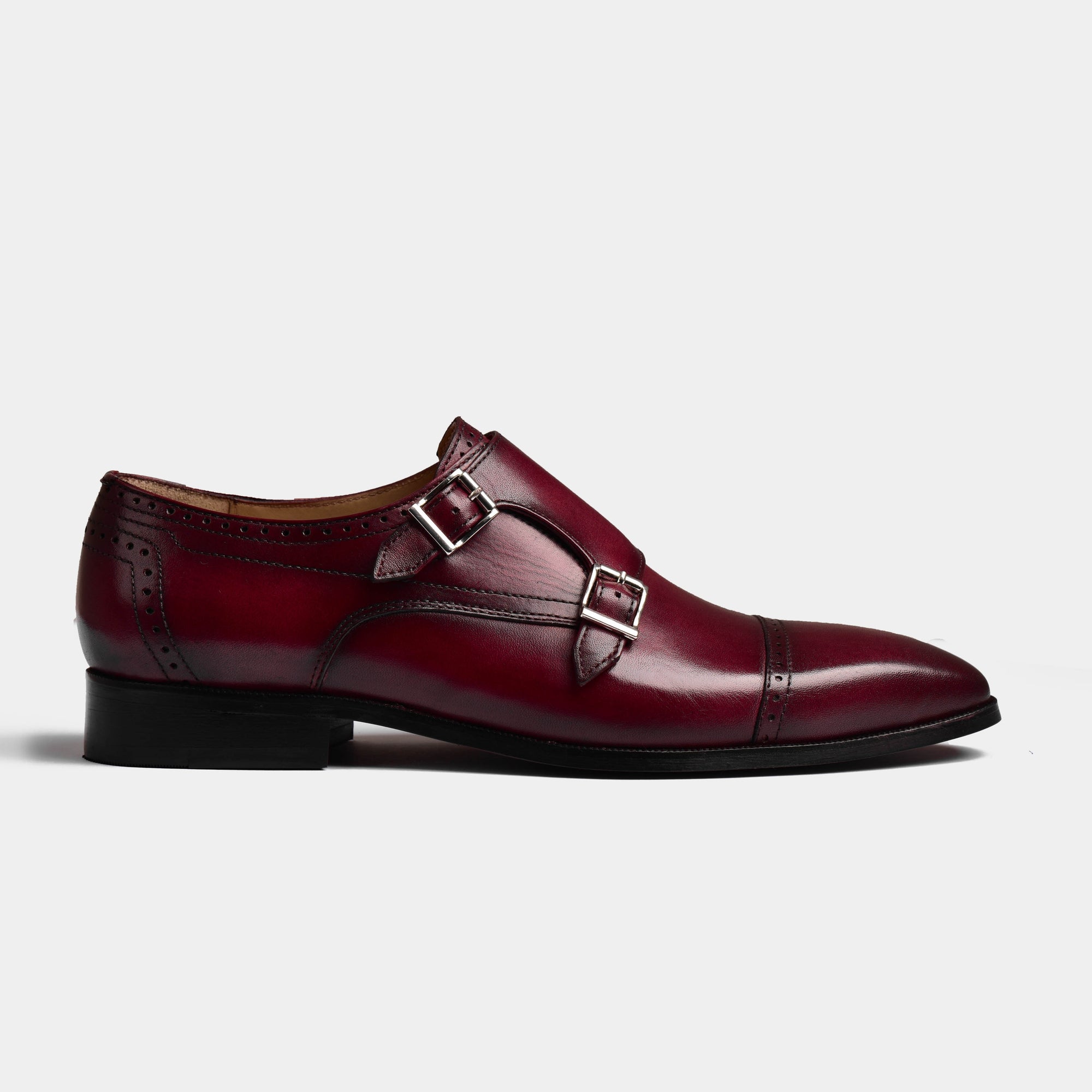 Side view of a men's Tabor Ruby Leather Monk Strap shoe, featuring a rich burgundy leather upper with broguing details and two silver buckles.