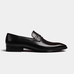 A side view of the Diaz Black Loafers, featuring a sleek black leather upper with a textured accent across the vamp and a silver-tone buckle detail.