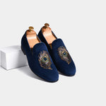 Pair of navy blue Artemio slip-on shoes with embroidered peacock feather designs on the toes.