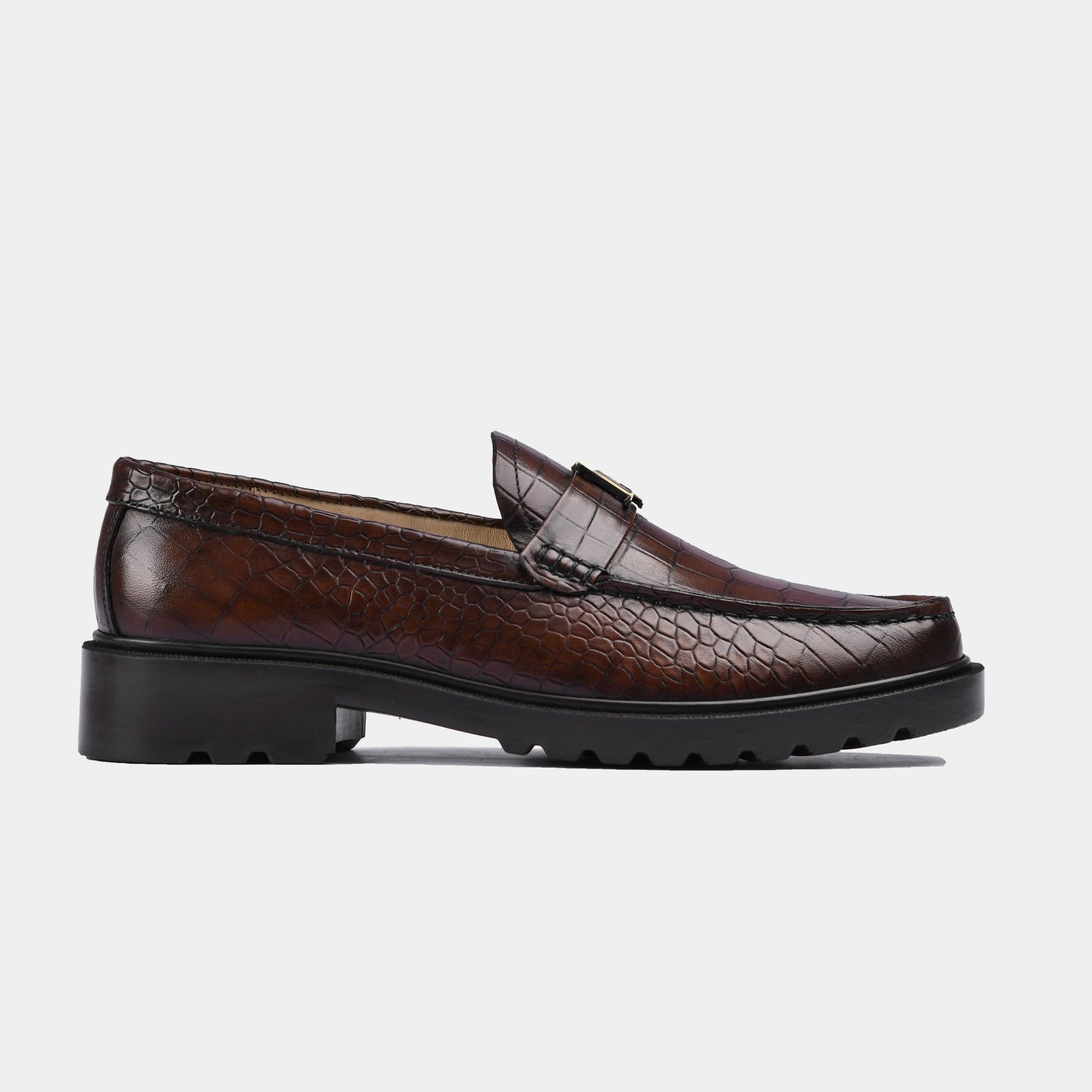 Pair of brown crocodile textured leather loafers, featuring a metal accent on the strap, and a chunky sole.