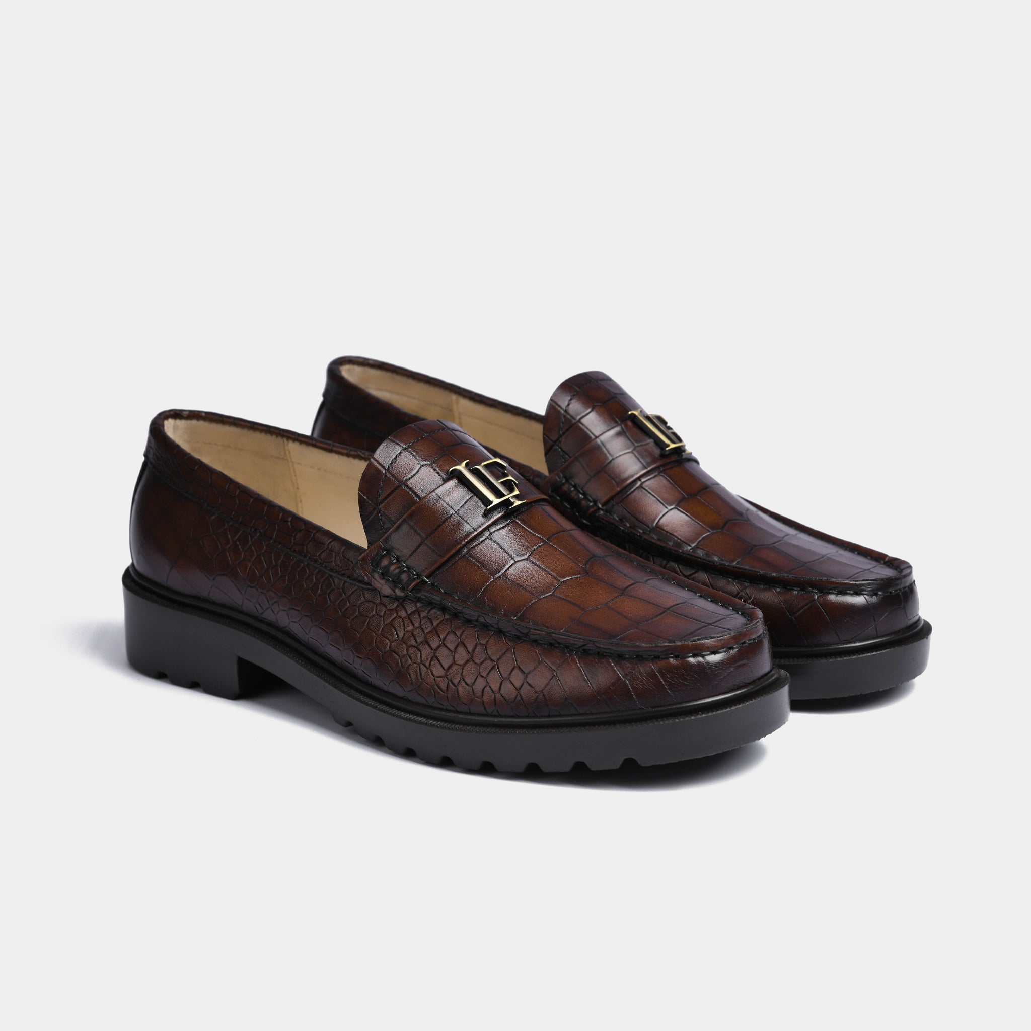 Pair of brown crocodile-textured leather loafers for men with a gold metal accent on the upper.