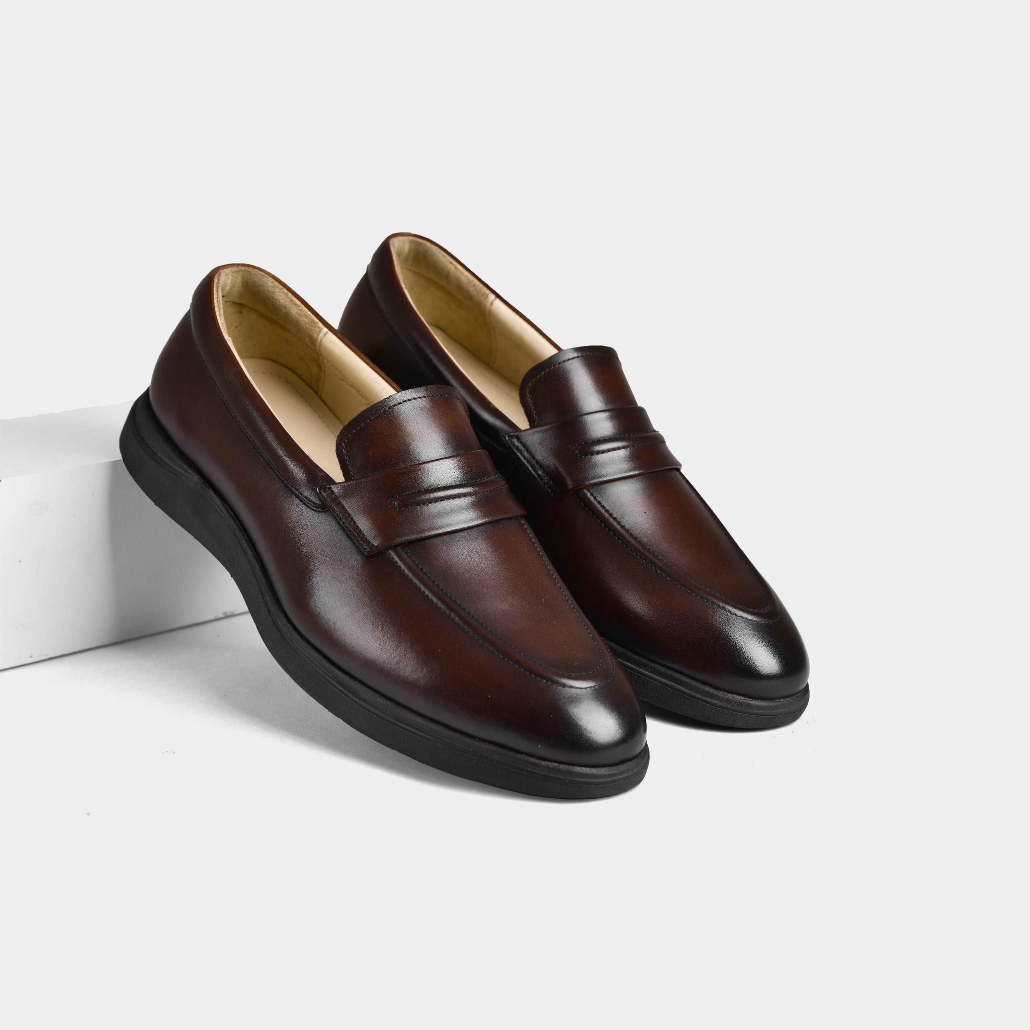 A pair of brown penny leather slip-on shoes with flexible black soles.