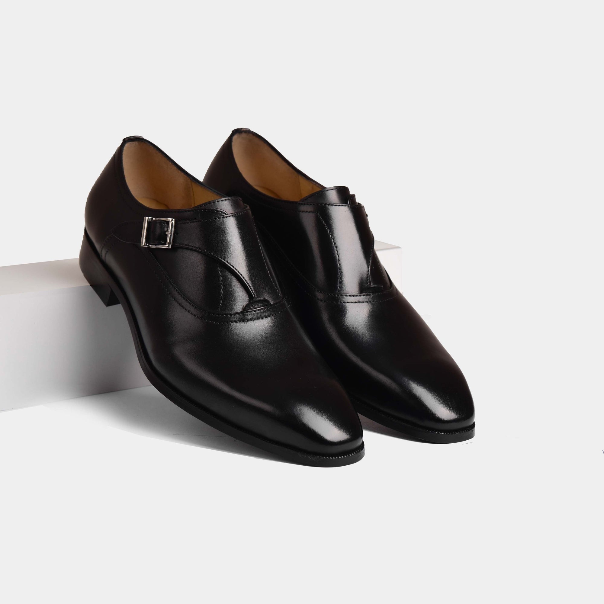 A pair of Reina Black Monk Straps, crafted from polished black leather, showcasing the signature buckle closure.