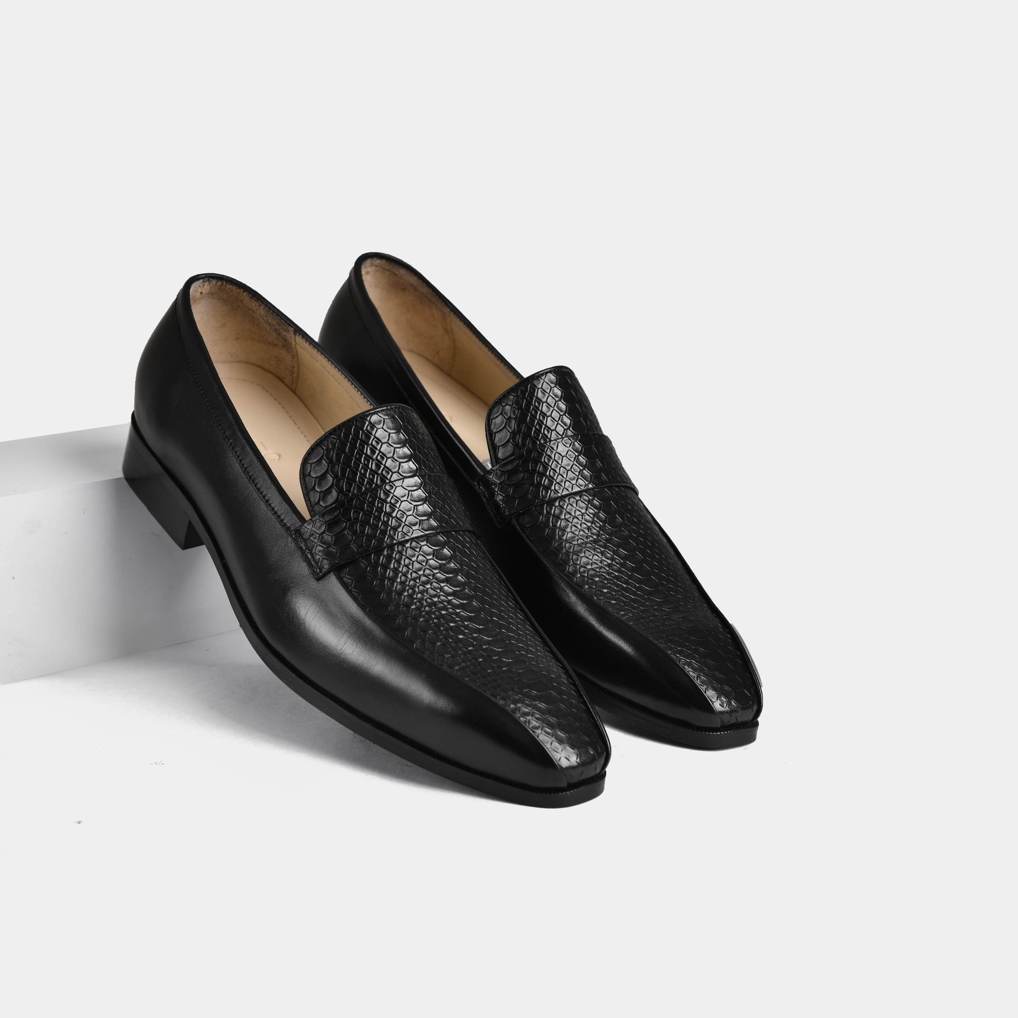 Pair of black leather penny loafers with snakeskin detail on a white background.