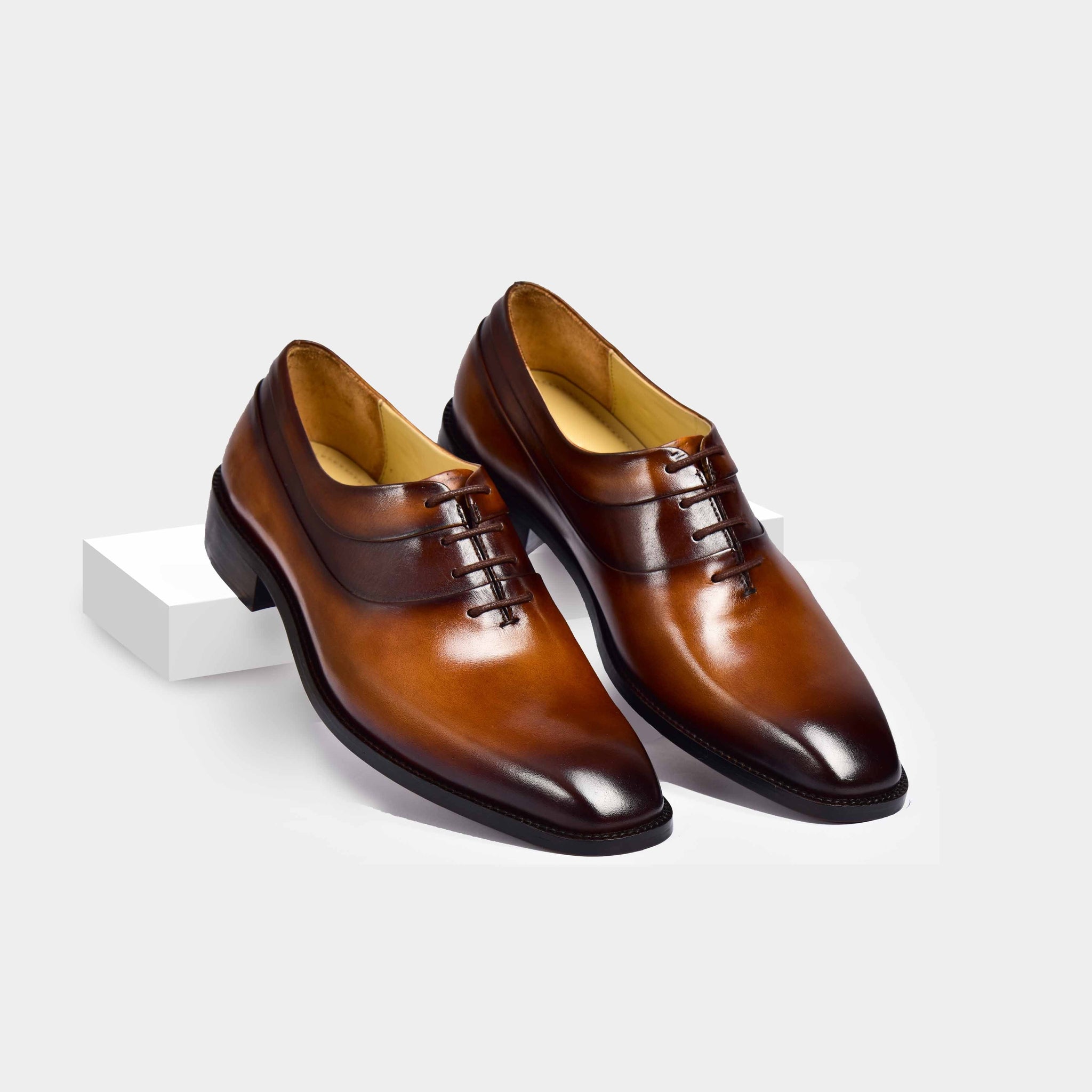 A pair of Charles Cognac Tan Leather Laceups, crafted from polished cognac-brown leather, stand on a white surface.