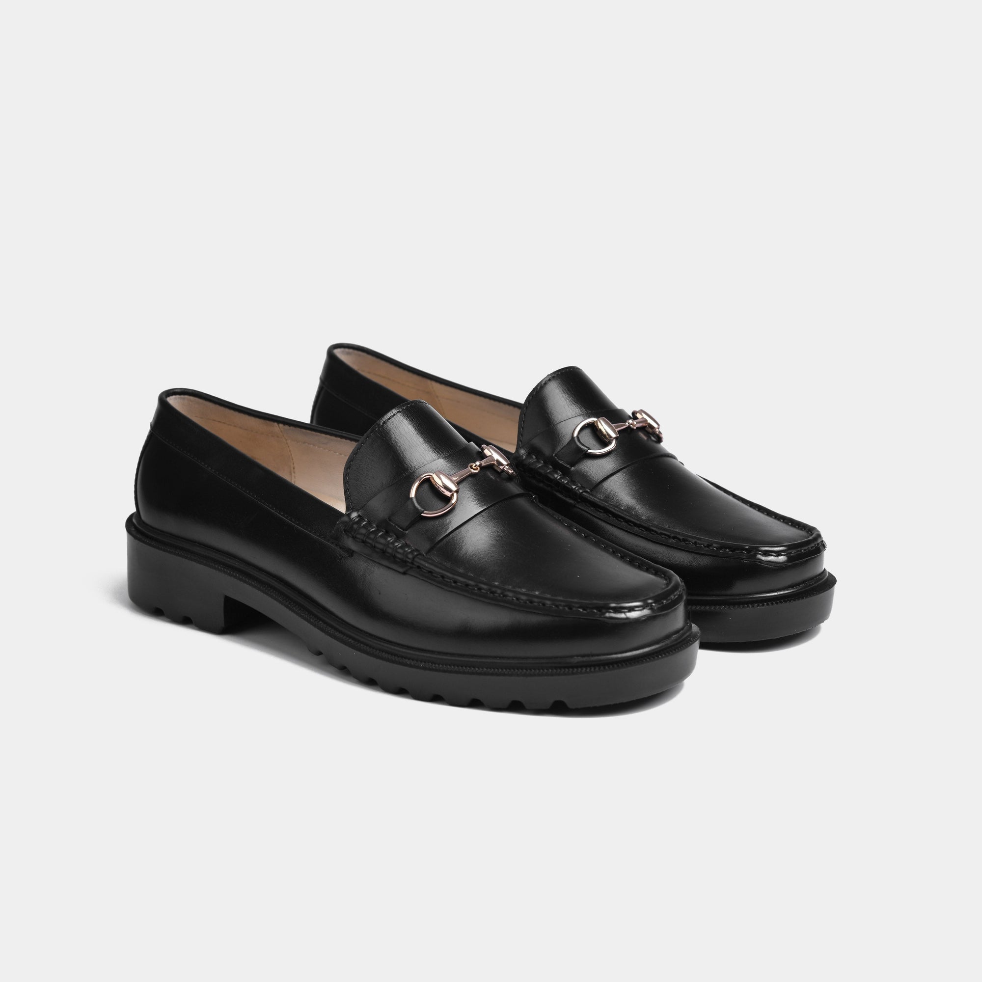 Pair of black leather loafers with gold snaffle bit hardware and chunky black soles.