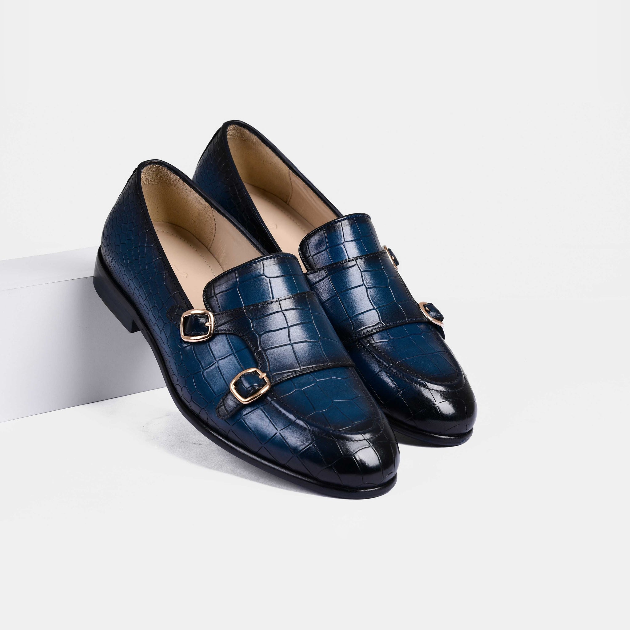 Pair of Valeria Croc Blue Leather Monk Strap shoes with double buckles on white background.