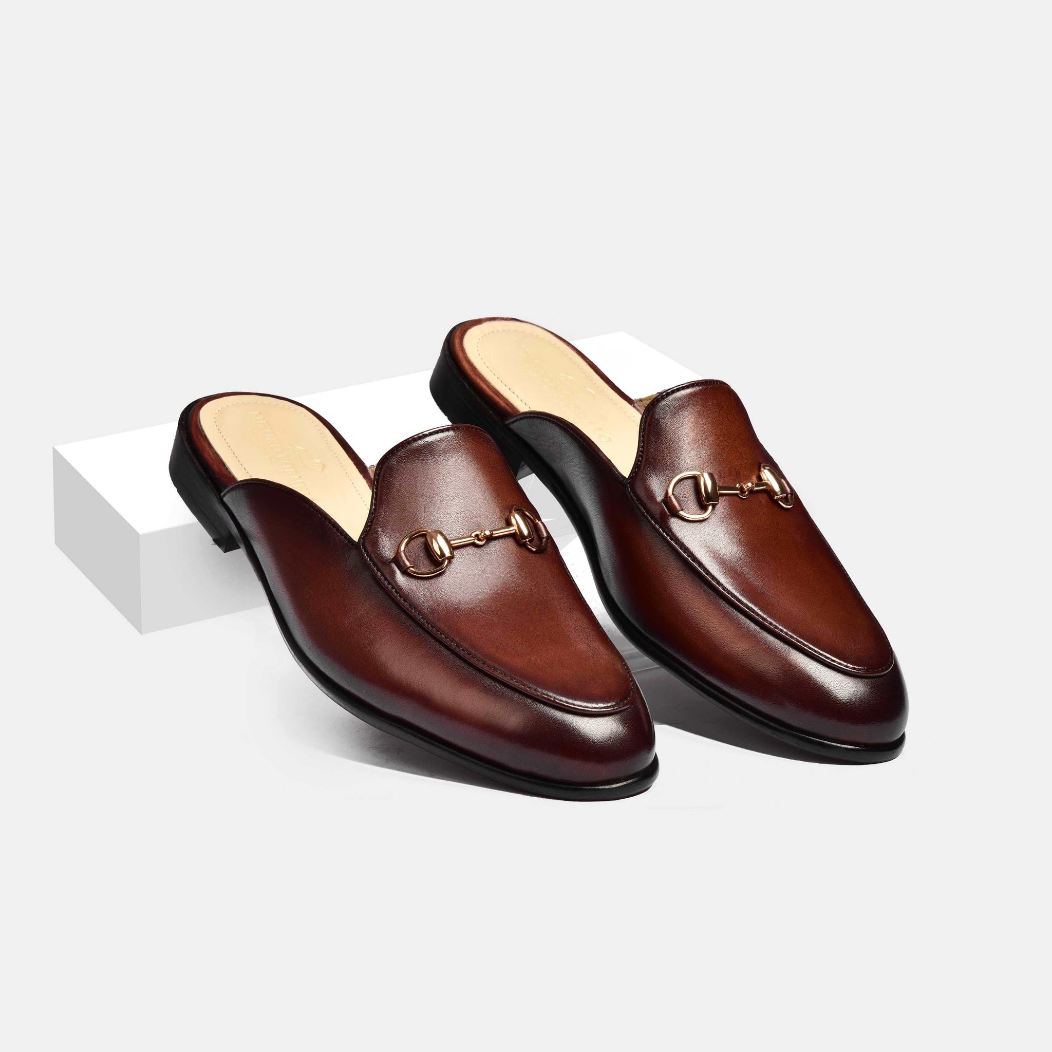 Pair of Arno brown leather mules with gold metal trim detailing, shown from a side view.