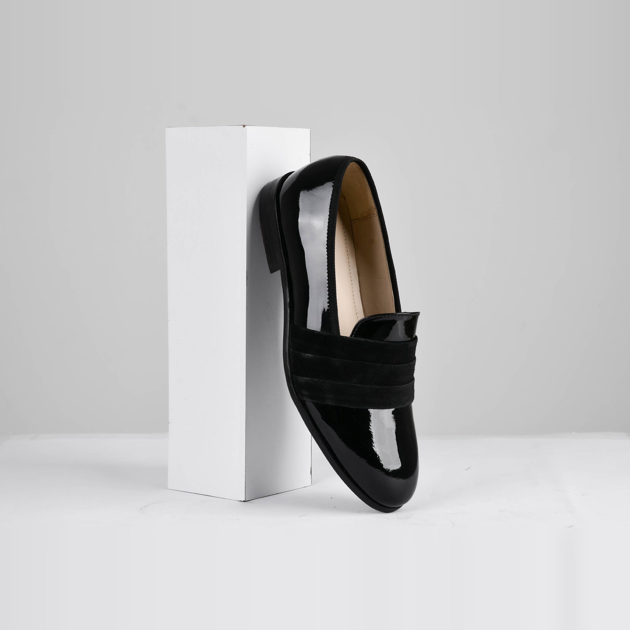 A single Delmar Black Patent Loafer with a black suede strap angled against a white cube.