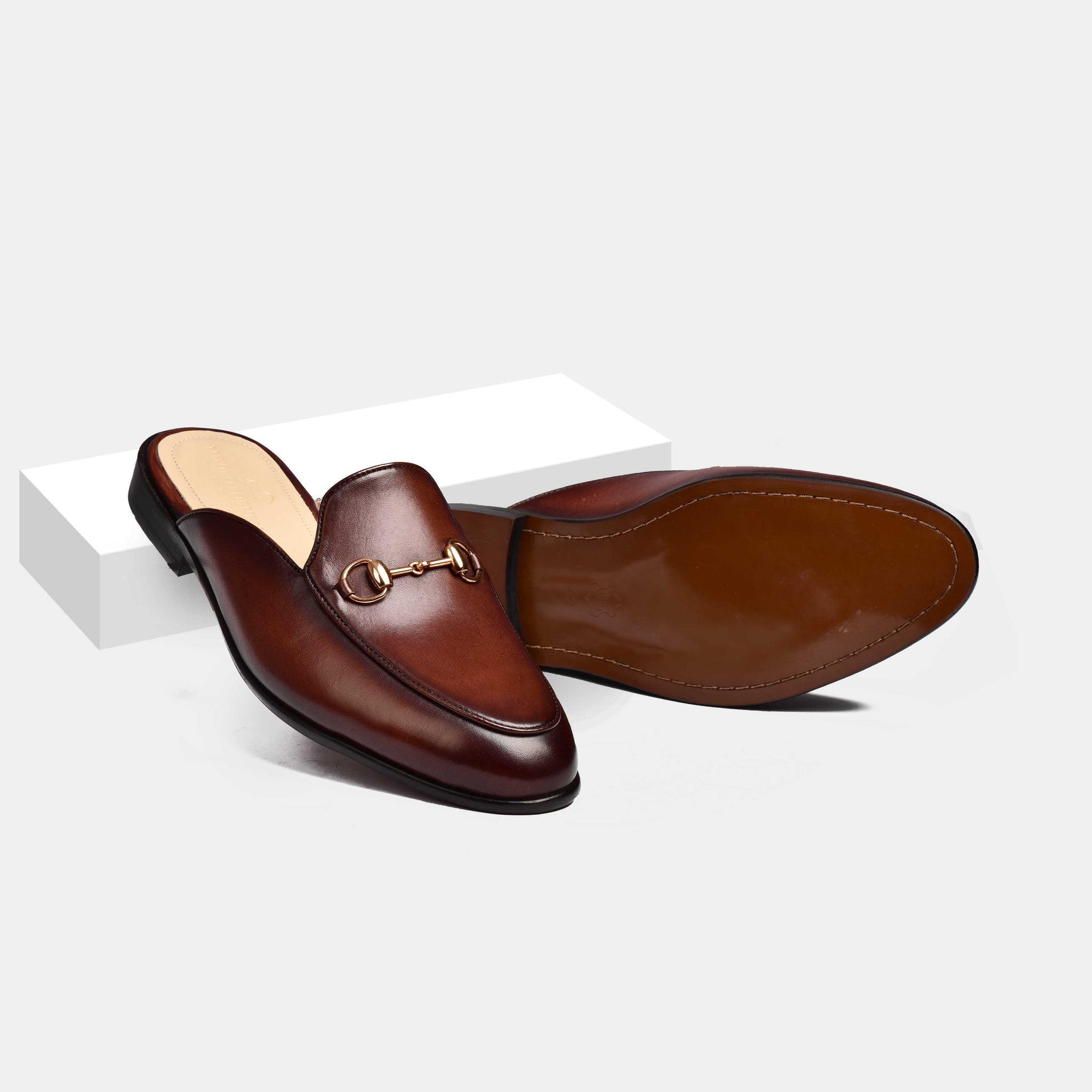 Pair of Arno Brown Formal Leather Mules with gold metal trim, shown from the side on a white surface.