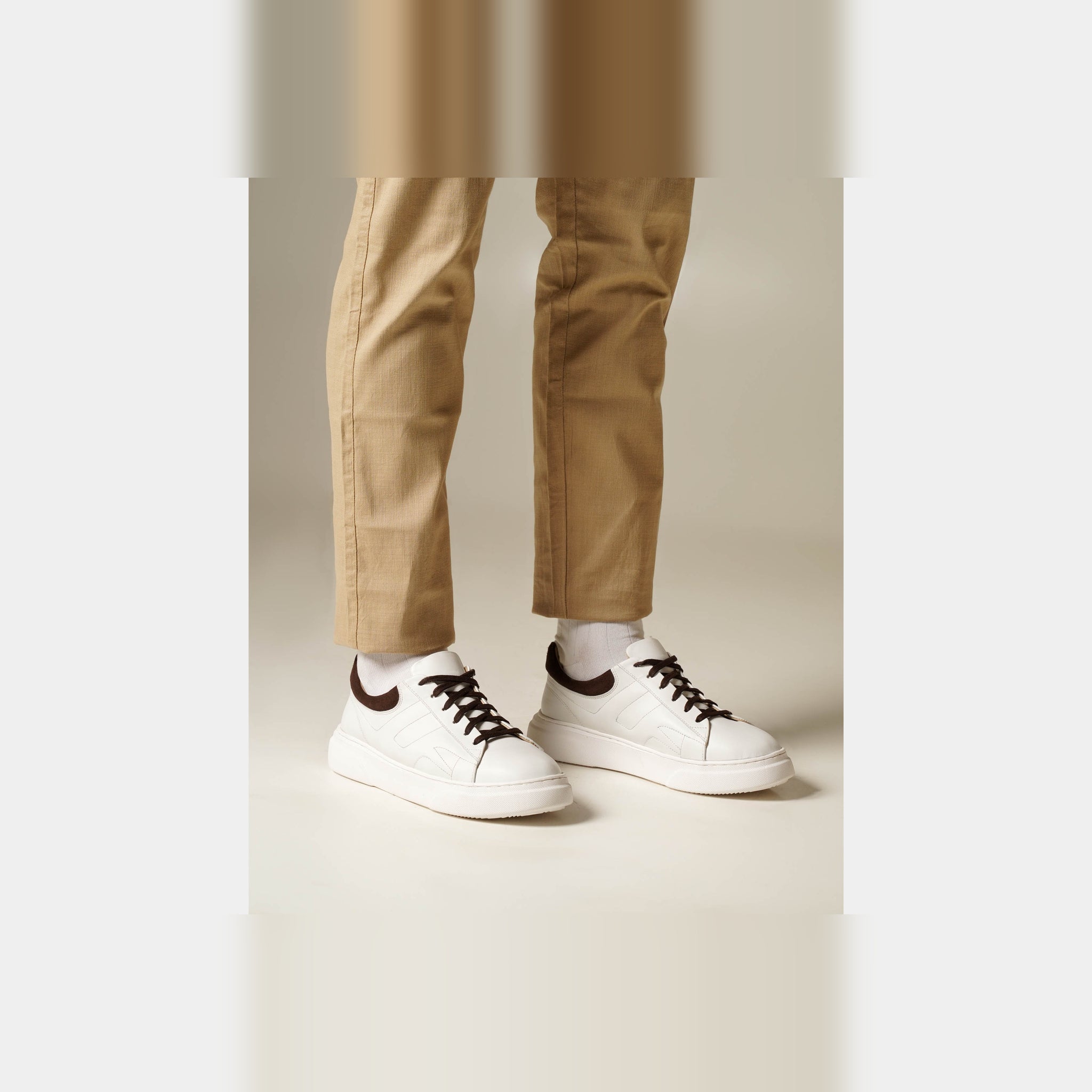 Man wearing white lace-up sneakers with brown accents and white socks. Perfect for casual and semi-formal looks.