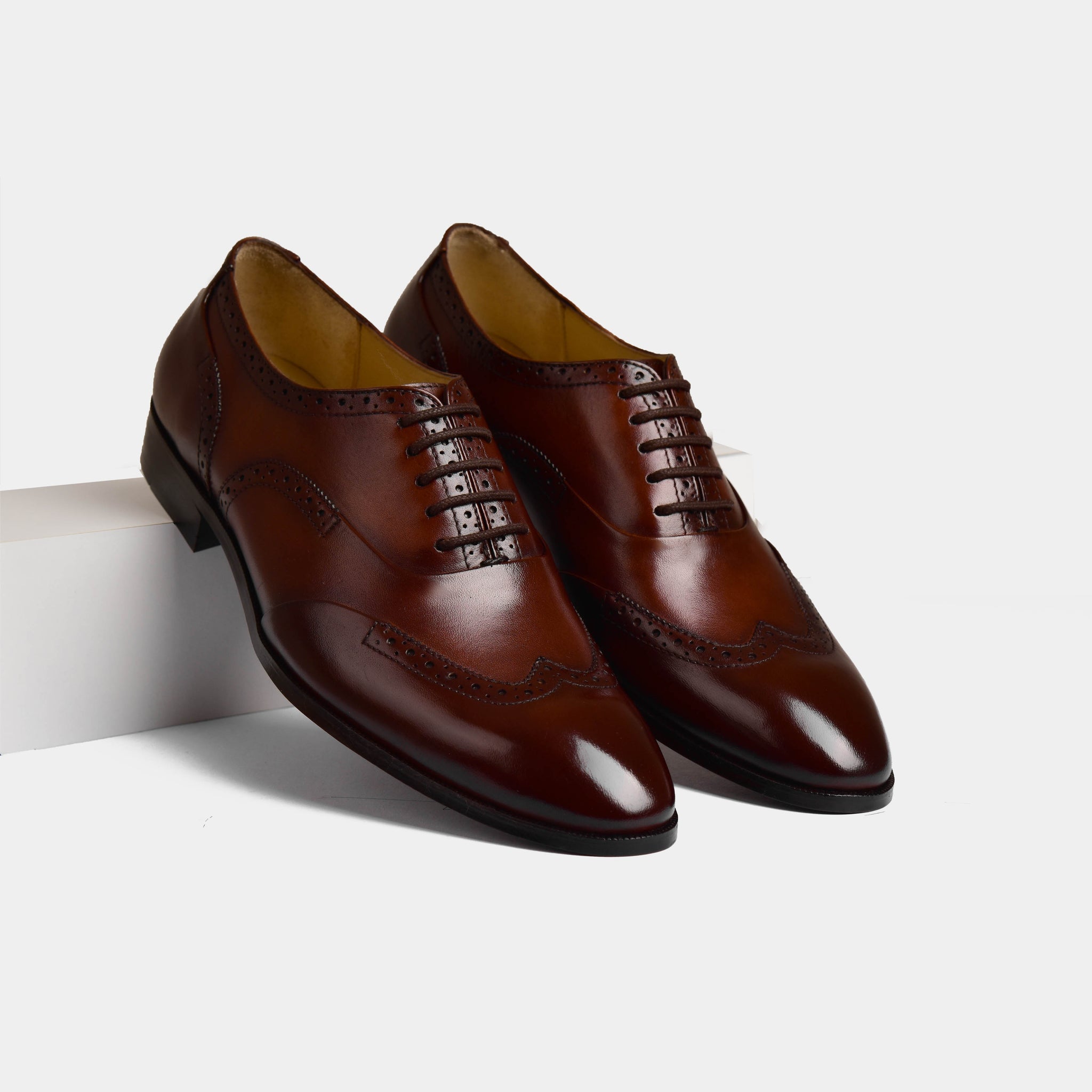 Pair of Kanor Tabaco Leather Laceups, brown dress shoes with brogue detailing, on white background.