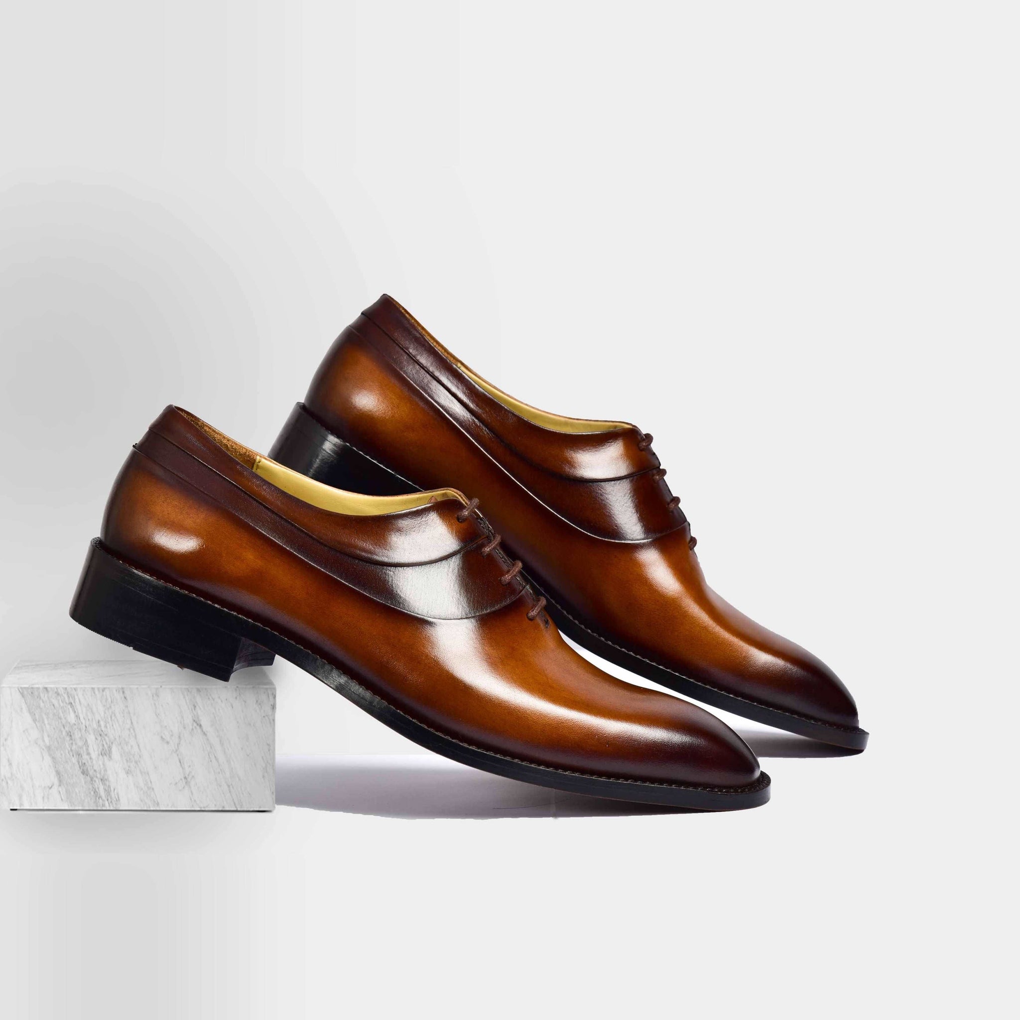 Pair of Charles Cognac Tan Leather Laceups, a stylish men's dress shoe in burnished cognac leather, resting on a marble block.